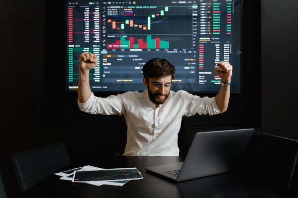 A man with his arms above his hands looking at a computer with stocks